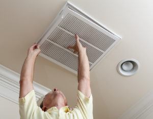 Man reaching up to open filter holder for air conditioning filter in ceiling